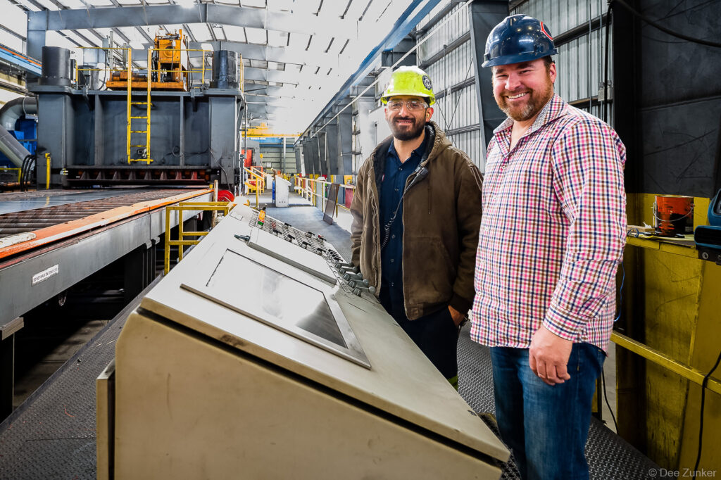 Two workers in hard hats smile beside industrial control panel at Industrial facility in Houston, TX.
