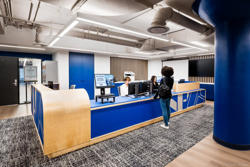 Students at a modern blue and wood reception desk inside the University of Houston-Downtown library, photographed by Dee Zunker Photography.