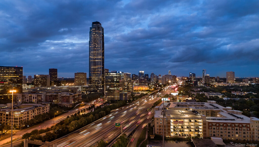 Aerial drone photo of the Williams Tower in Houston's Galleria area at twilight. Clouds backdrop the skyscraper and West Loop traffic.