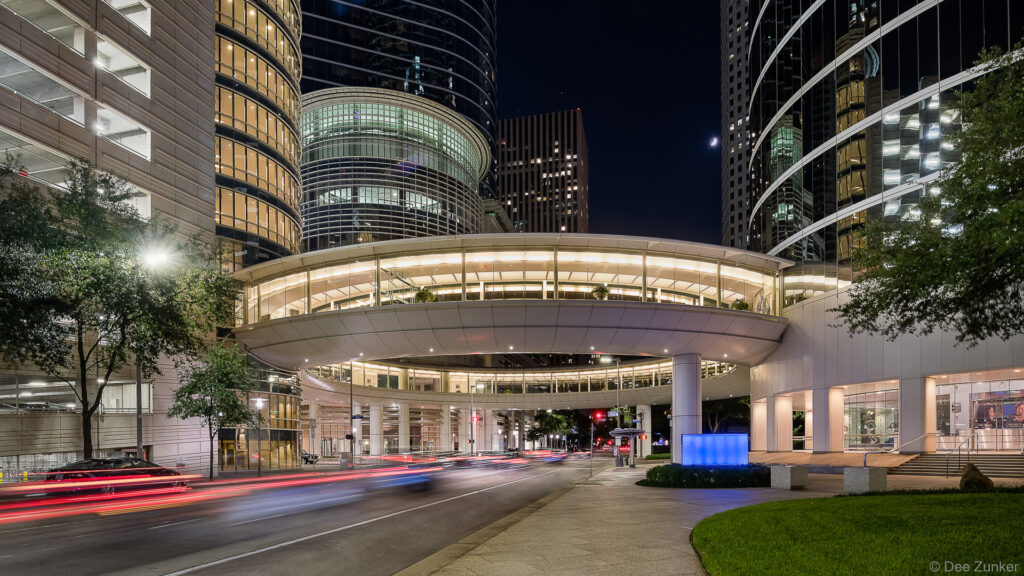 Nighttime exterior of a curved glass office tower at 1300 Smith Street Houston with light trails from passing traffic