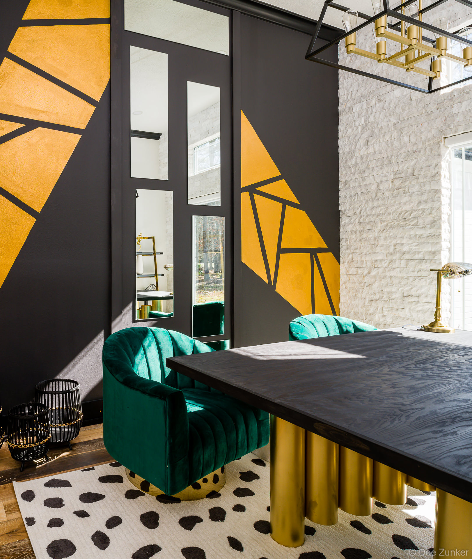 Dramatic commercial interior in Huffman TX featuring emerald velvet chairs, black table with brass legs, and geometric gold mural wall art.