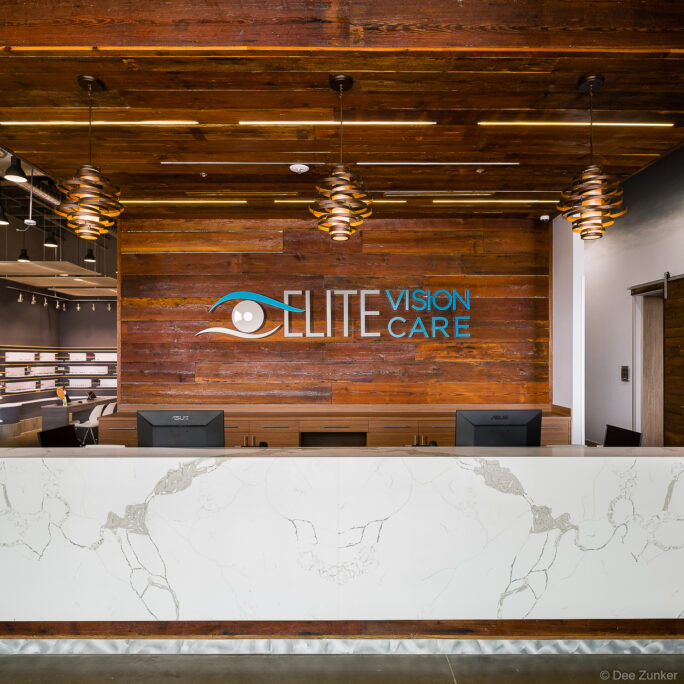 Interiors photo of Elite Vision Care in Pearland, TX. The front counter features white marble, set against a distressed wood ceiling and backwall.