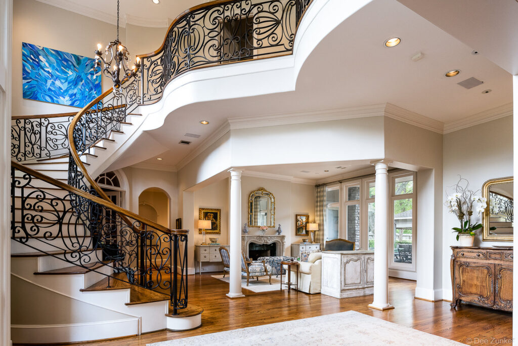 Sweeping wrought-iron staircase with wood handrail in grand two-story foyer at Bellaire residential interior photography.