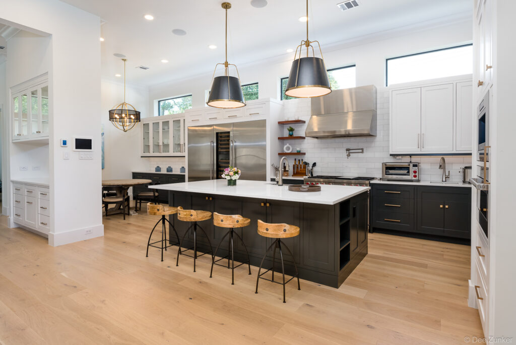 Luxury Houston kitchen with dark ebony cabinetry, white quartz island, brass pendant lights, and wood barstools over light hardwood floors.