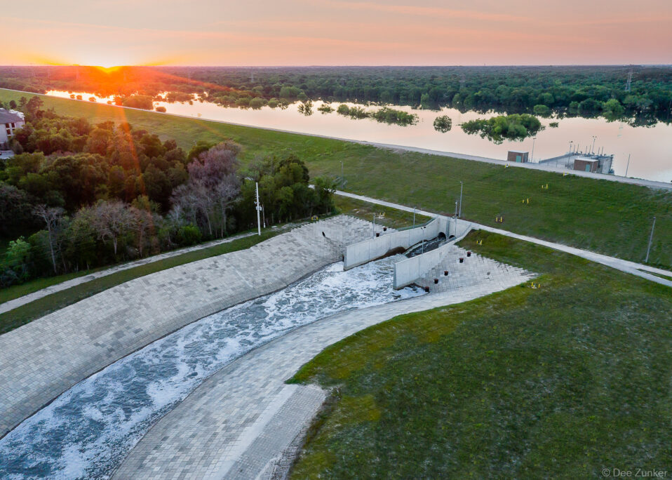 Aerial drone photo of Addicks Reservoir dam spillway releasing water at sunset, Houston flood control infrastructure, Texas.
