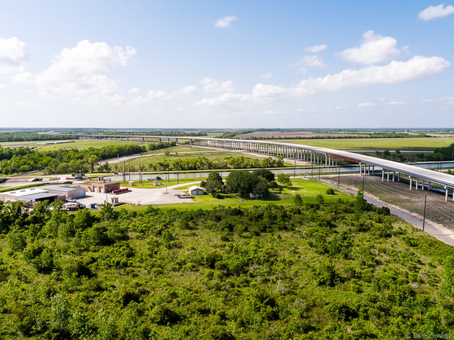 Drone aerial photo of Highway 99 elevated bridge spanning a canal through flat green Texas farmland, shot for infrastructure portfolio.