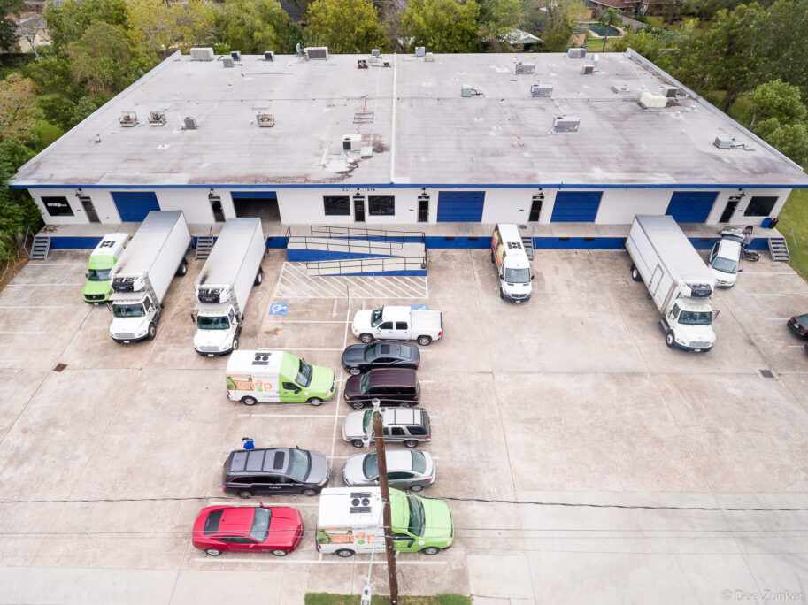 Drone aerial photo of Houston warehouse facility with delivery trucks, refrigerated vans, and parking lot, exterior commercial photography.