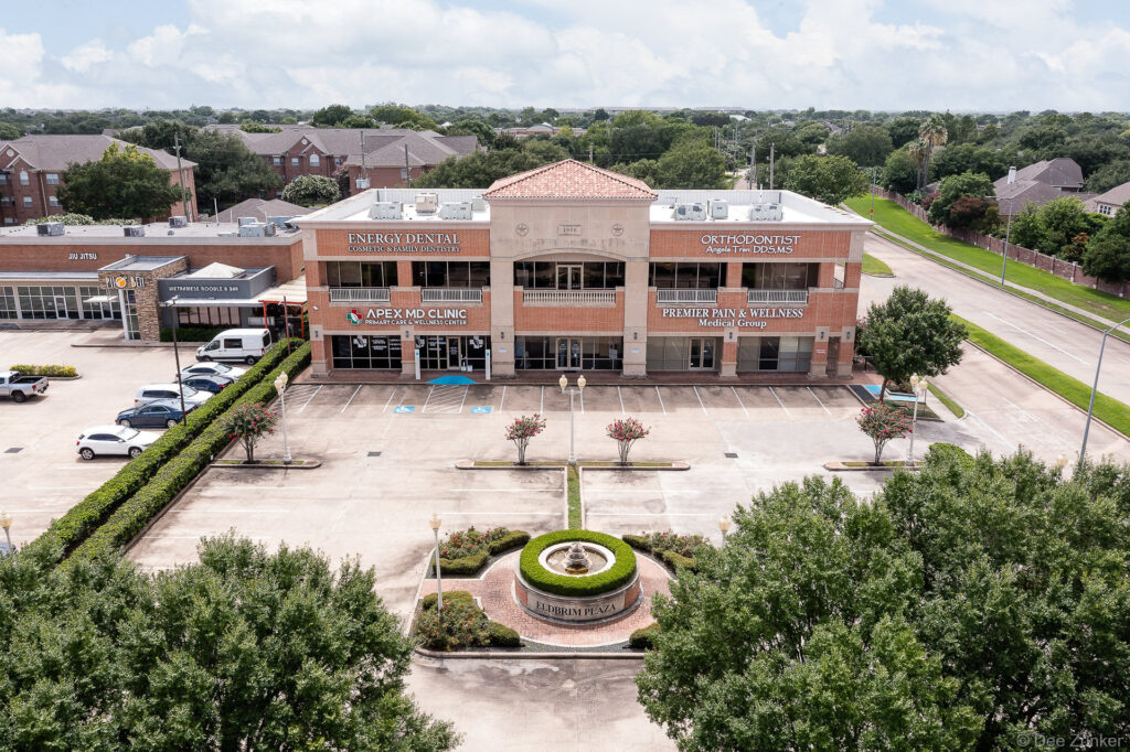 Drone aerial photo of a two-story brick medical and dental office plaza with fountain courtyard and parking lot in Houston, TX.