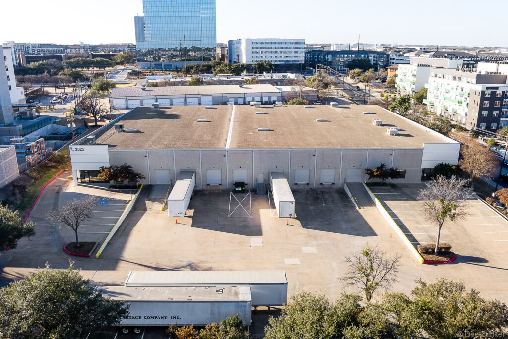 Drone aerial photo of a large industrial warehouse with loading docks and parking lot in a Dallas urban commercial district.