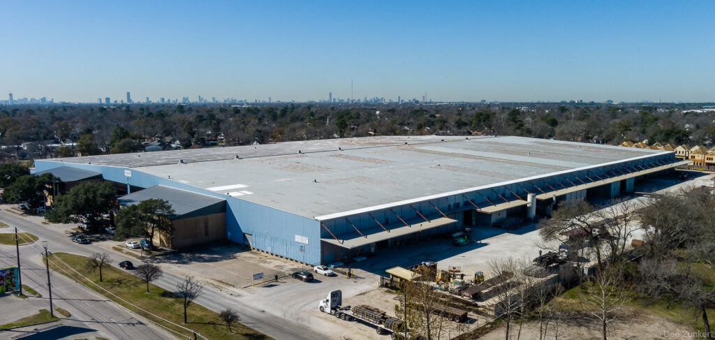 Drone aerial photo of a large industrial warehouse facility near Houston TX with loading docks and city skyline in background.