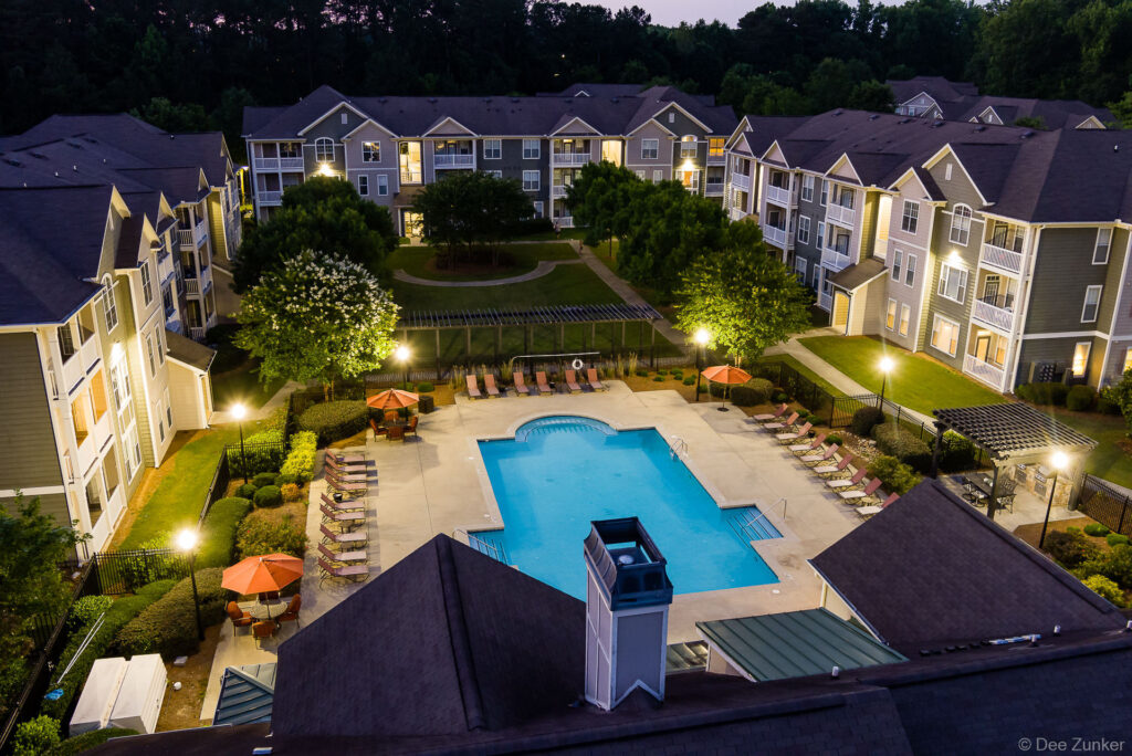 Aerial twilight view of apartment complex pool deck with lounge chairs, umbrellas, and landscaped courtyard, Georgia