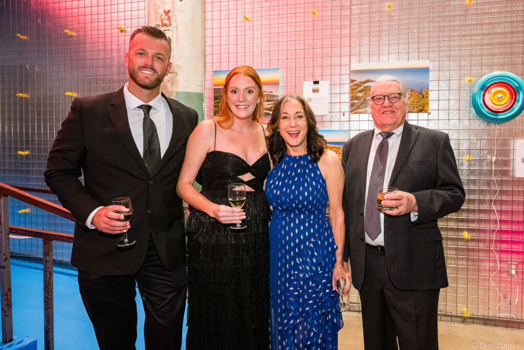 Four formally dressed corporate event attendees smiling and holding drinks at the AIAH Gala in Houston, TX.
