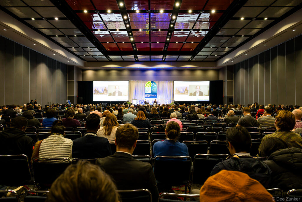 Packed conference ballroom at AMS Annual Meeting with attendees facing large projection screens and a panel on stage.