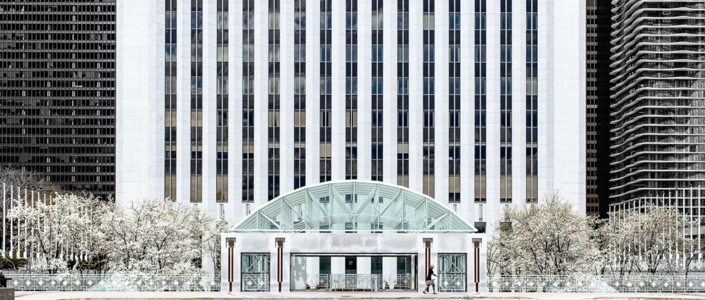 Exterior architectural photography of a large white office tower with glass canopy entrance and flowering trees in Chicago