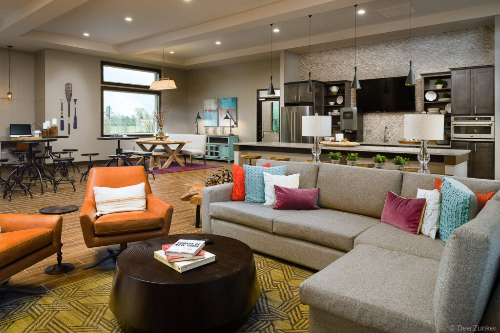 Modern apartment community room with sectional sofa, colorful accent pillows, leather chairs, and open-plan kitchen amenity, Houston