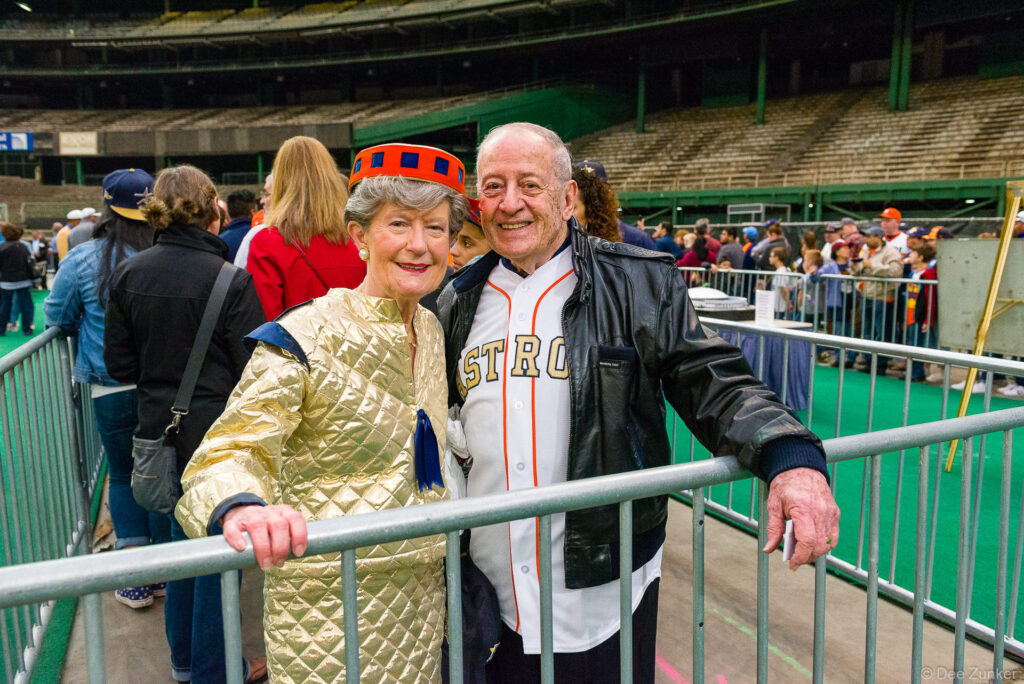 Two smiling attendees in Astros jersey and gold costume pose at the Domecoming event inside the Houston Astrodome.