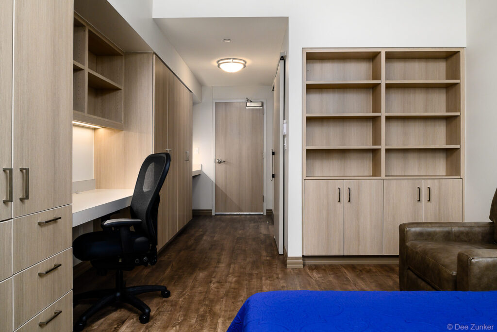 Modern student housing bedroom with built-in desk, shelving, wardrobe, ergonomic chair, and blue bedding at Axis St Marys Houston.