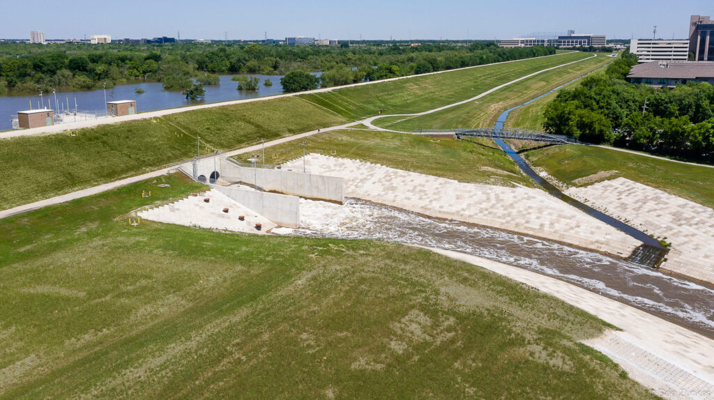 Aerial drone photo of Barker Reservoir flood control outlet structure with concrete spillway channels and grassy levee, Houston, TX.