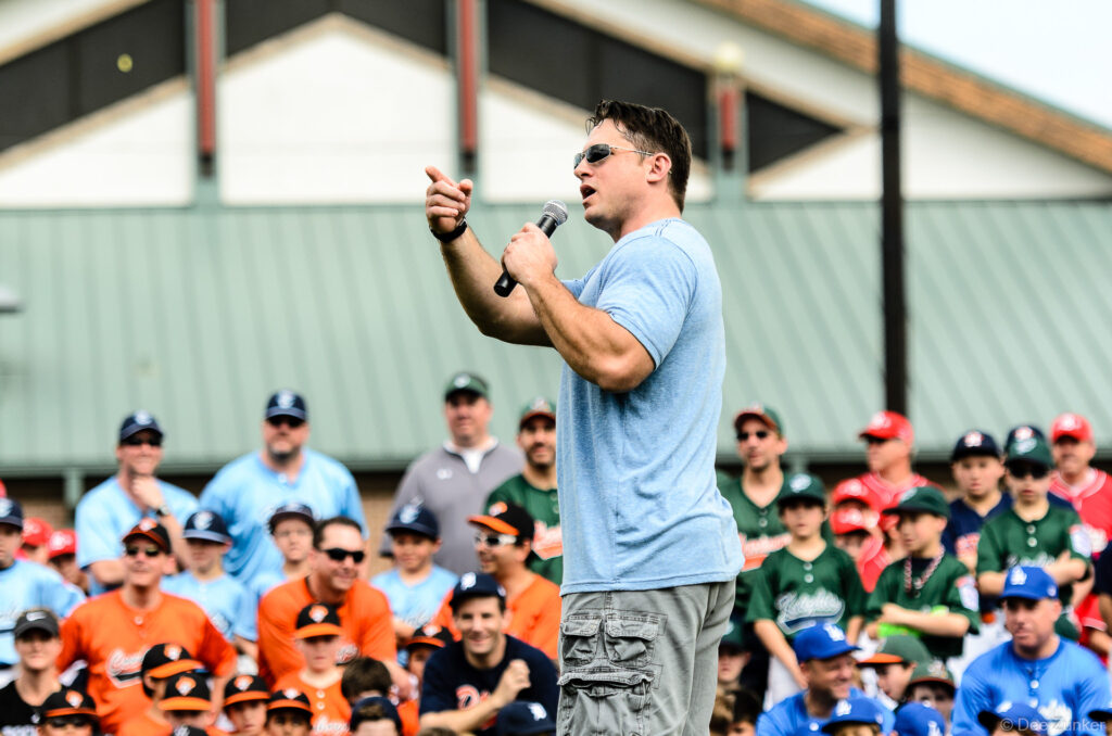 Male speaker addresses youth baseball players and coaches at an outdoor opening day ceremony, Houston corporate event photography 2014.