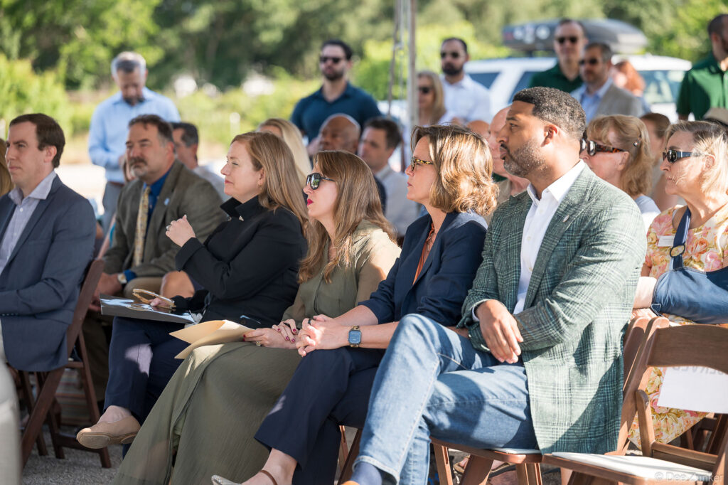 Attendees seated in folding chairs at an outdoor groundbreaking ceremony near Cypress Ditch in Bellaire, Houston, Texas.