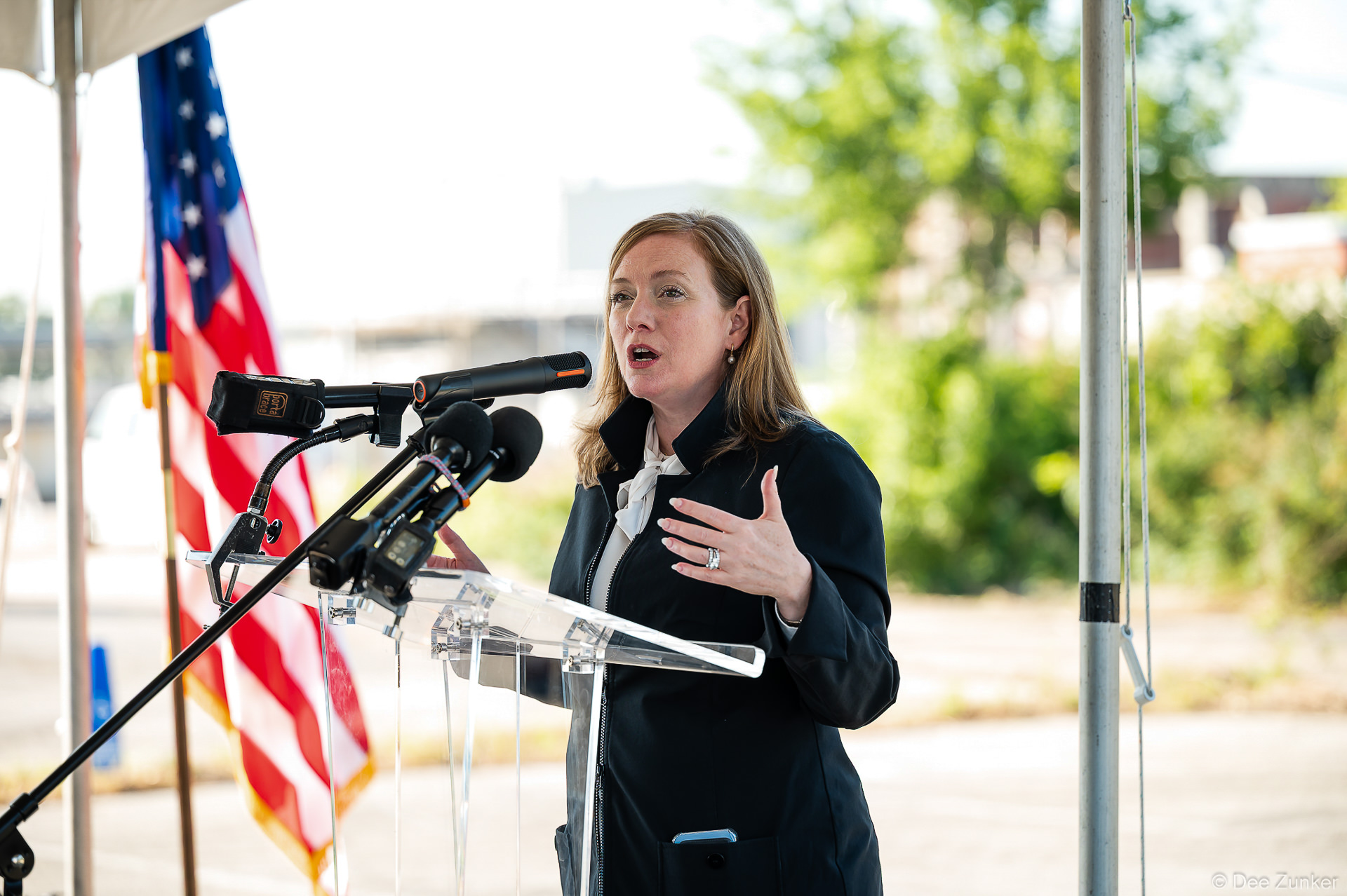 Woman speaker addresses podium with microphones at Bellaire Cypress Ditch groundbreaking ceremony, Houston corporate event photography.