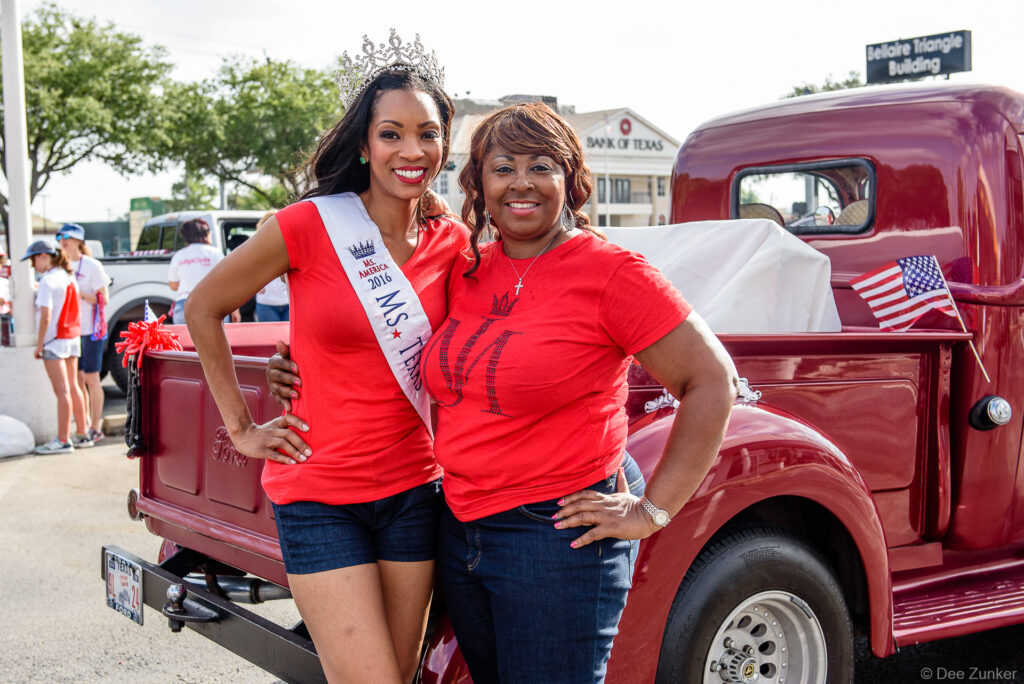 Ms America titleholder wearing crown and sash poses with supporter beside vintage red Ford truck at Bellaire Fourth of July Parade.