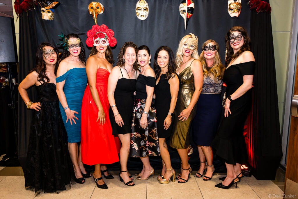 Nine women in formal gowns and masquerade masks pose at a Bellaire Parks fundraiser gala in Houston