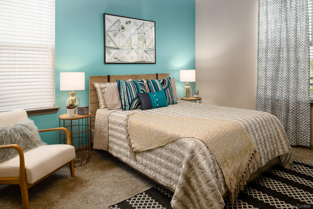 Styled apartment bedroom with teal accent wall, wood headboard, layered bedding, and decorative pillows at Boterra Bay Houston.