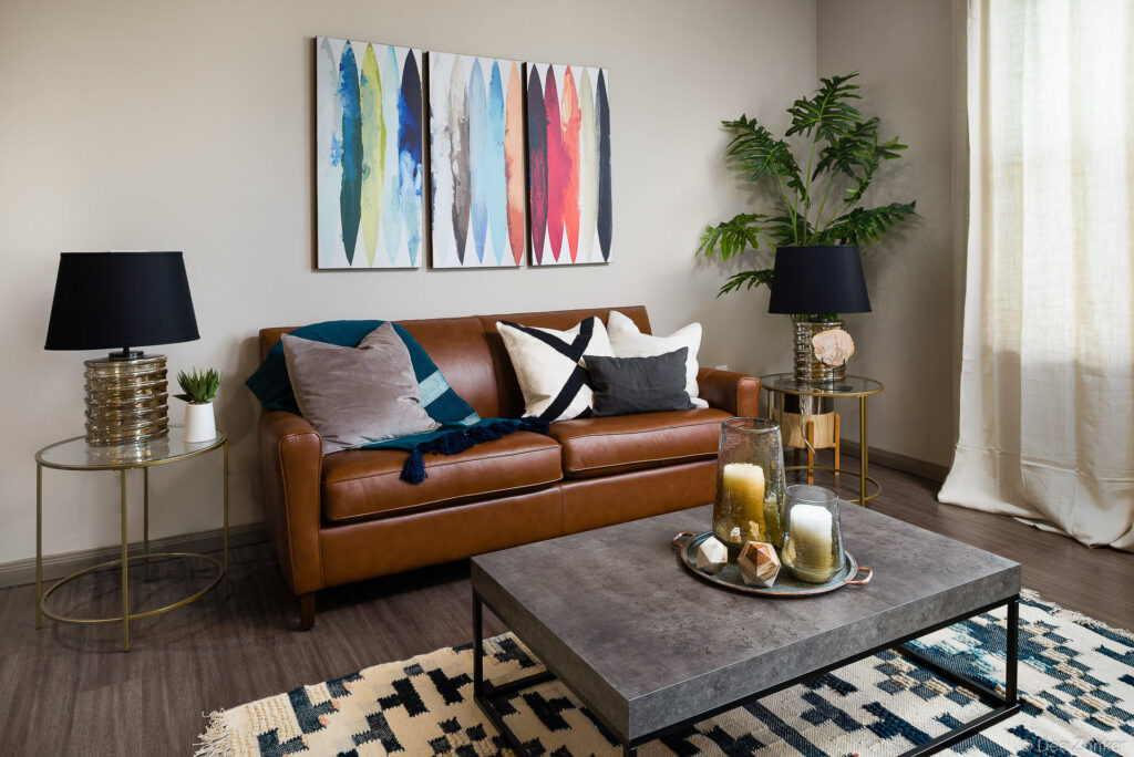 Staged model apartment living room with cognac leather sofa, abstract wall art, and modern coffee table at Boterra Bay Houston.