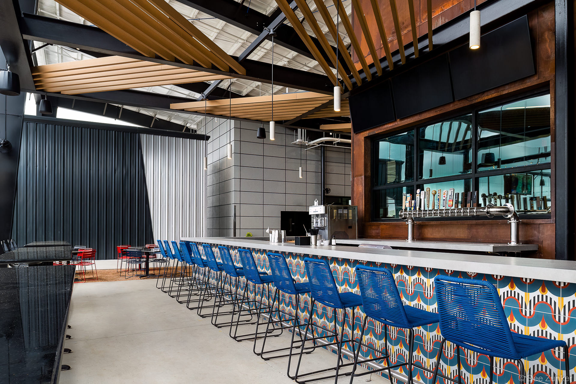 Modern brewery taproom bar with blue rope barstools, colorful geometric tile facade, draft taps, and wood slat ceiling in Katy TX