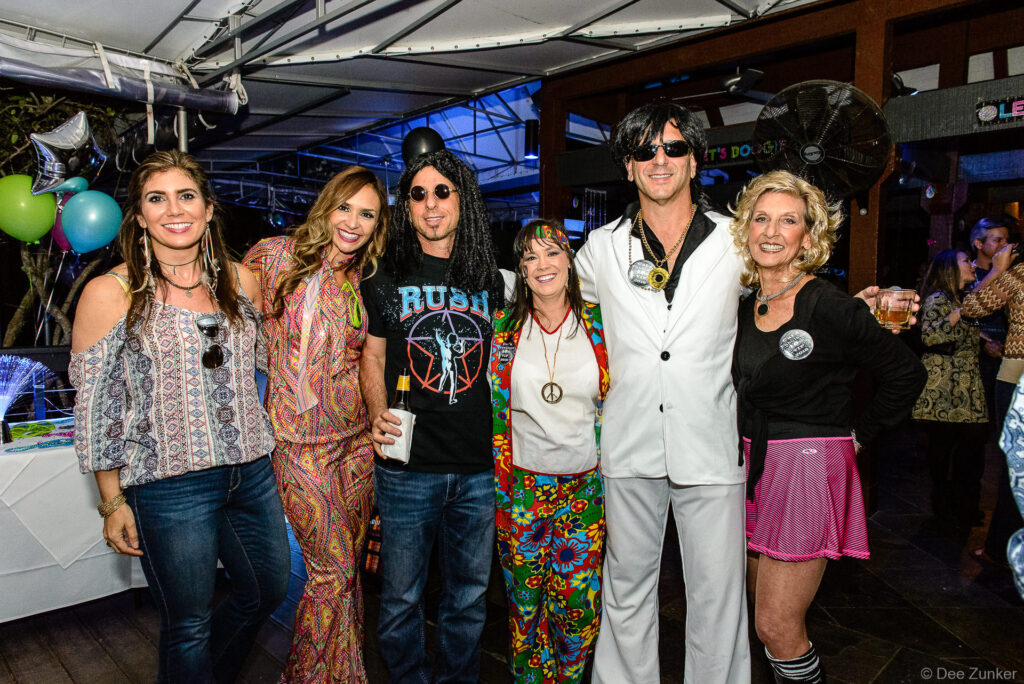 Group of six adults in 1970s themed costumes pose together at a Houston corporate birthday celebration event