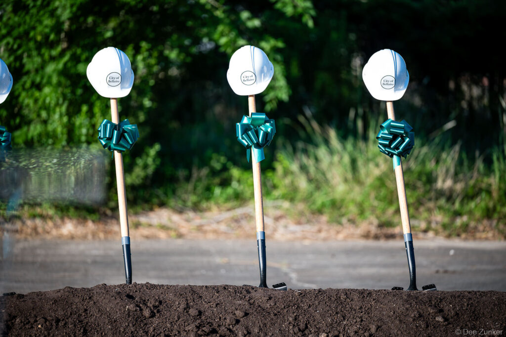 Decorated shovels with white hard hats and green bows stand in ceremonial dirt mound at a City of Bellaire groundbreaking event.