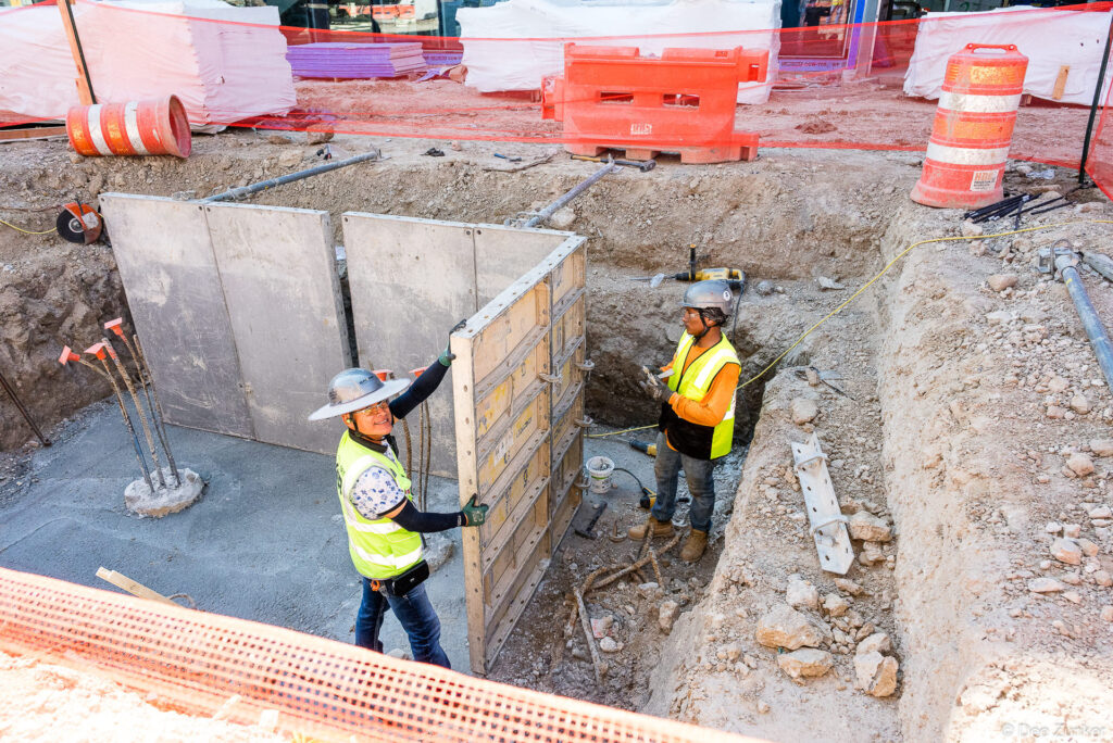 Two construction workers in high-visibility vests install trench shoring panels at the Clark IAH B Terminal jobsite in Houston.