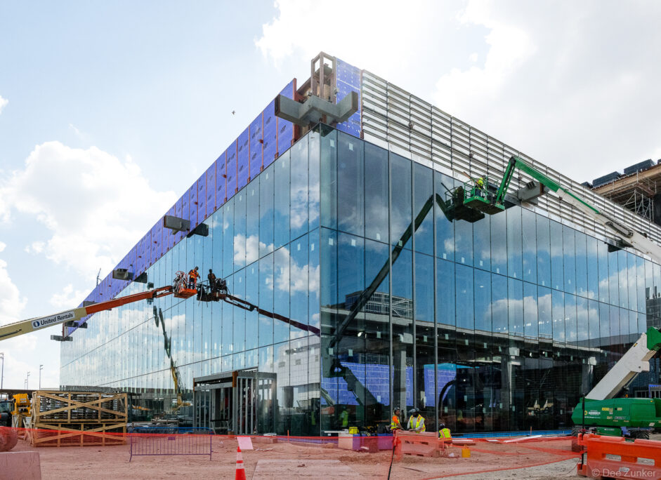 Workers on aerial lifts install glass curtain wall panels on the Clark IAH Terminal B exterior during active construction in Houston.