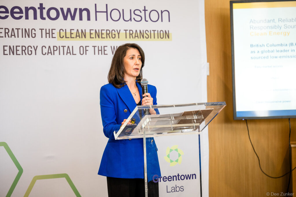 Woman speaker in blue blazer addresses clean energy transition conference at Houston innovation hub podium with branded backdrop.