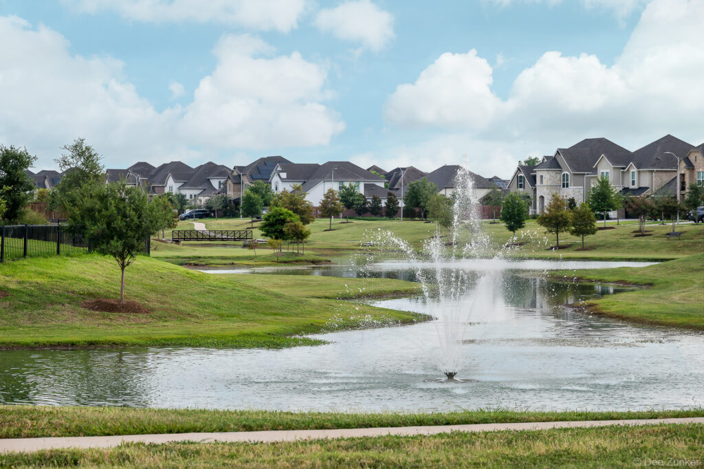 Decorative pond fountain at Clements Crossing residential community Houston TX, surrounded by green landscaped grounds and suburban homes.
