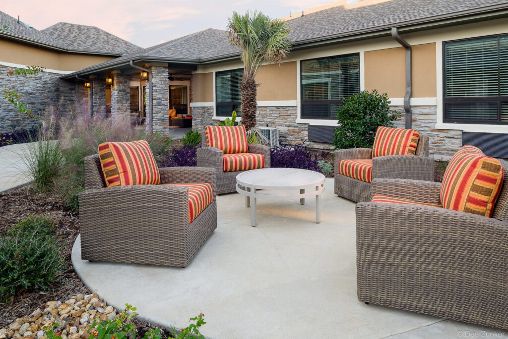 Wicker lounge chairs with striped cushions arranged around a white coffee table on a concrete patio at a College Station senior living facility.