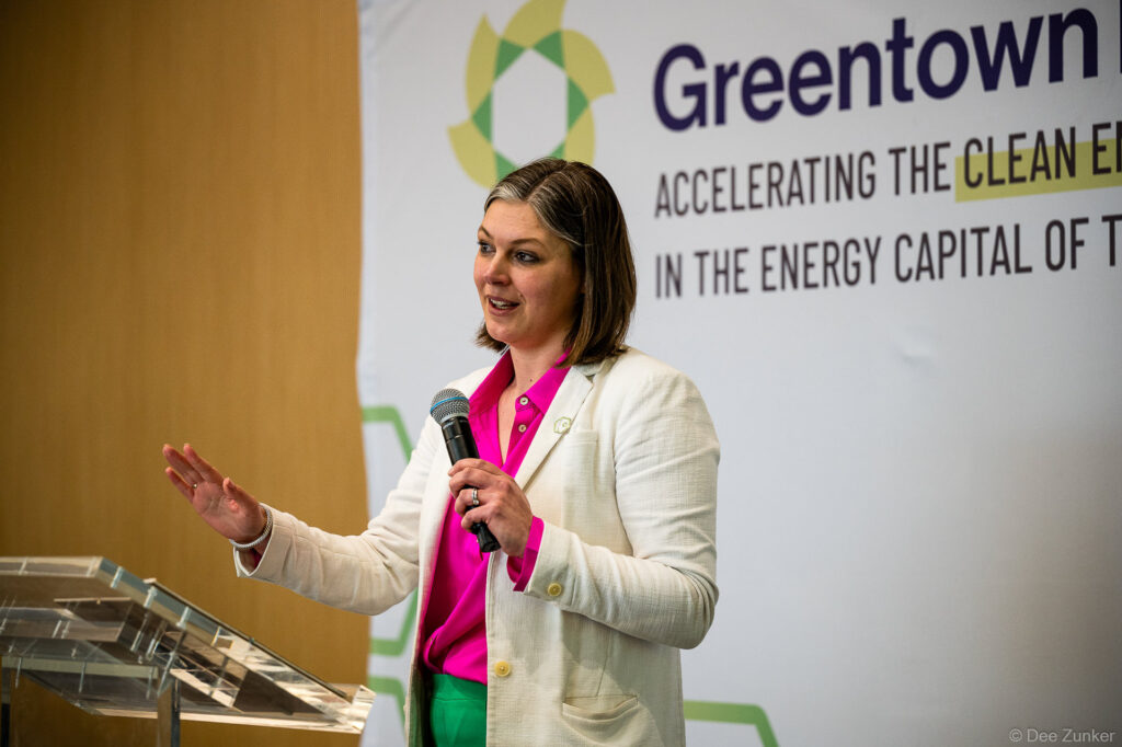 Female keynote speaker holds microphone and gestures on stage at Houston corporate conference event