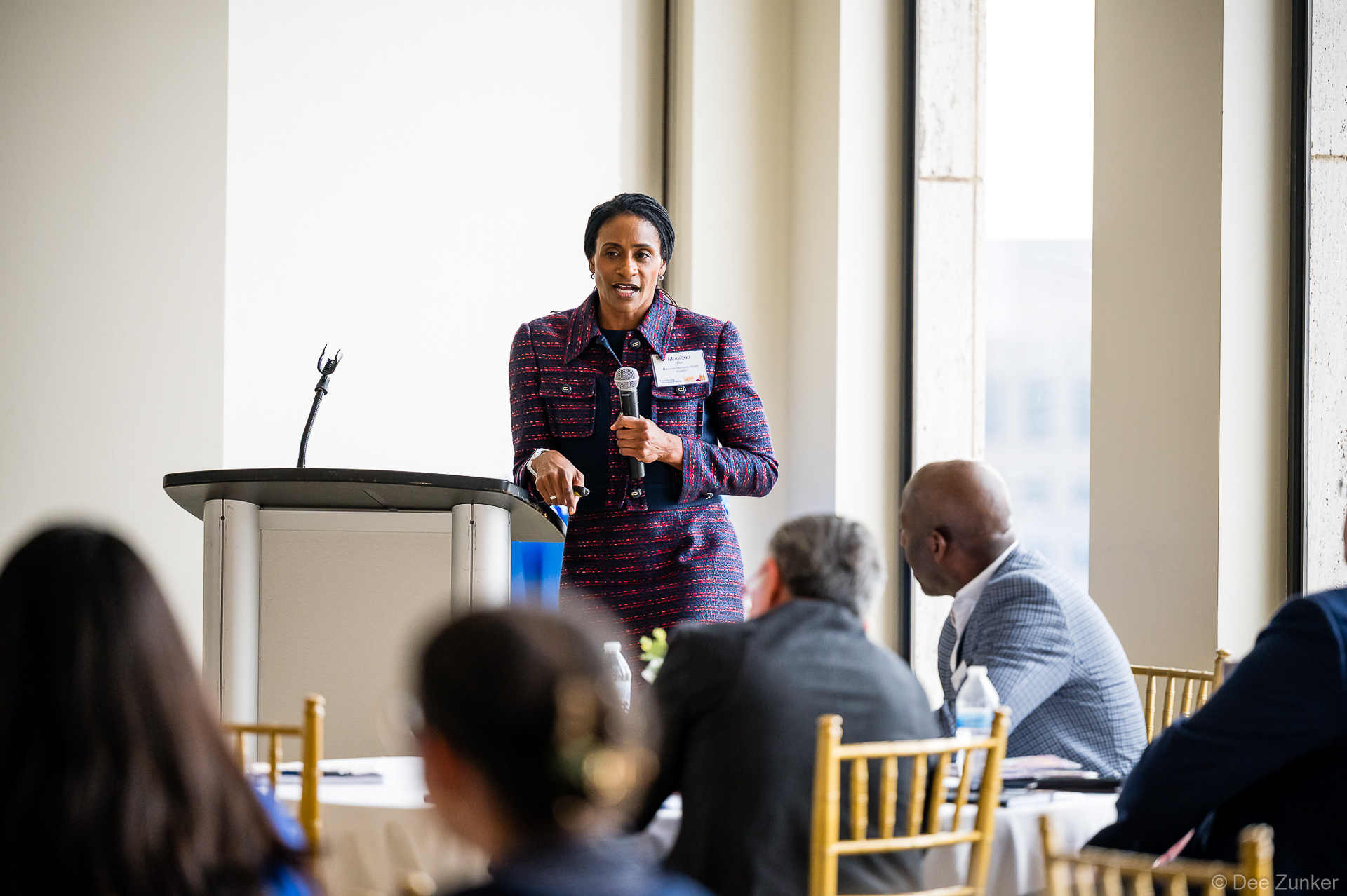 Female keynote speaker addresses corporate conference audience at podium holding microphone, Houston professional event photography