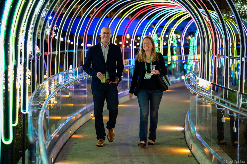 Two corporate event attendees walking through a colorful illuminated tunnel at a Houston opening reception