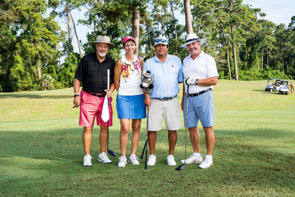 Four golfers posing together on a lush Houston golf course during a corporate golf tournament blowout event