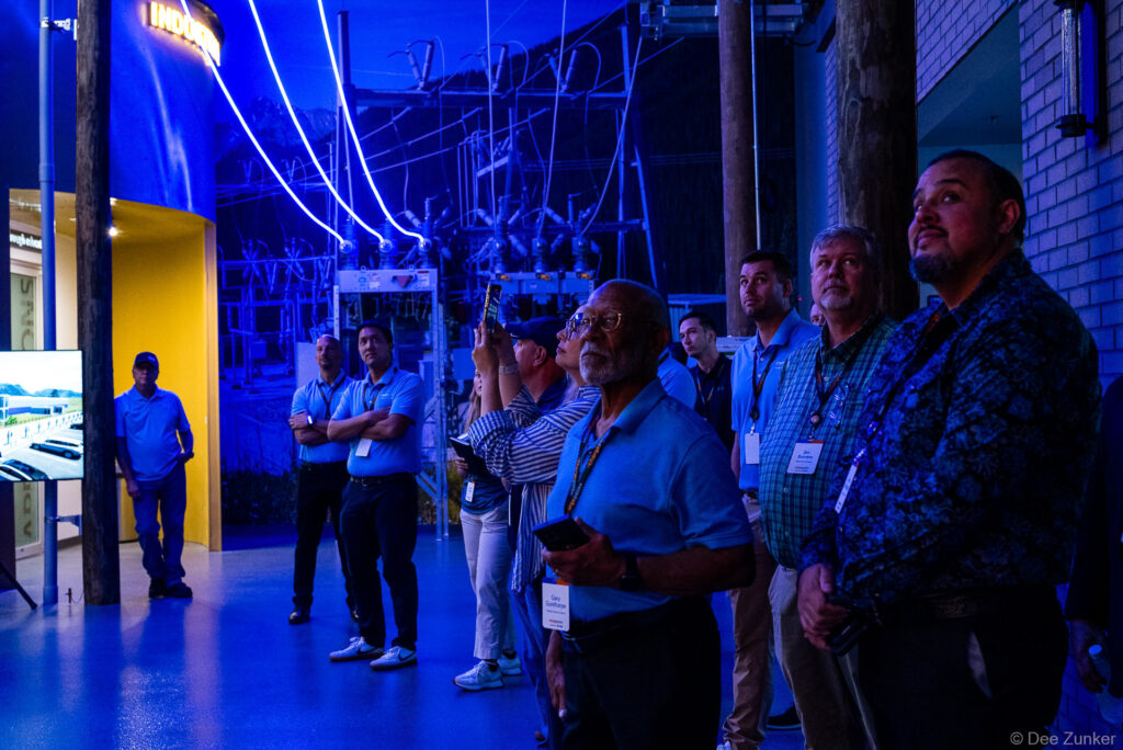 Group of corporate attendees in blue lighting look up at electric infrastructure display during a Houston industry facility tour.