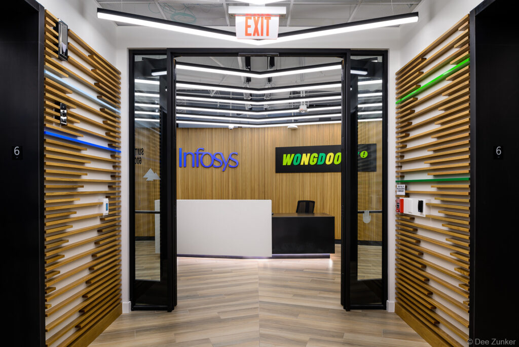 Modern corporate office entrance with wood slat walls, black glass doors, LED ceiling lights, and a sleek reception desk beyond