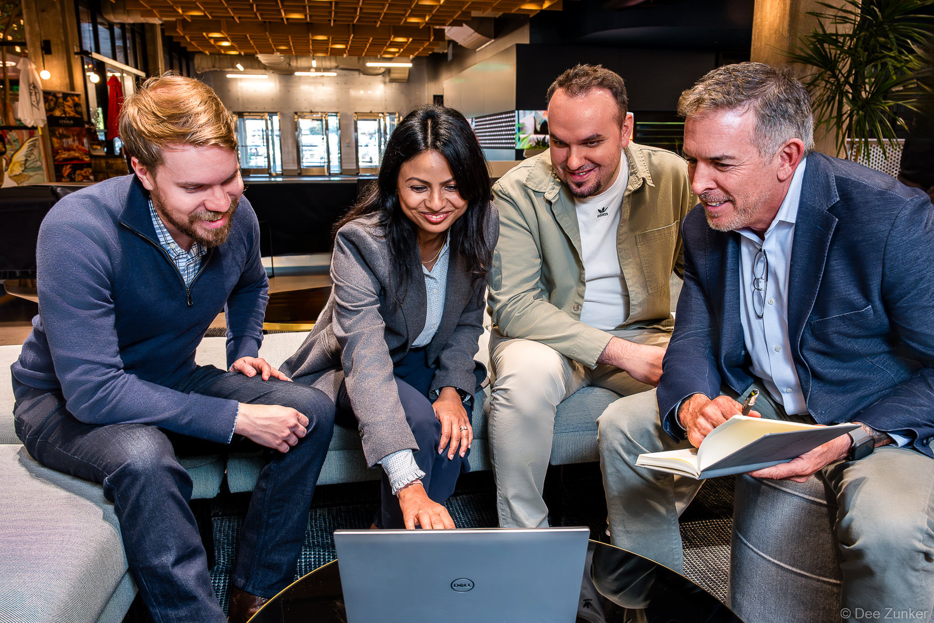 Four corporate professionals gathered around a Dell laptop in a modern Houston office lounge, smiling during a collaborative branding meeting.