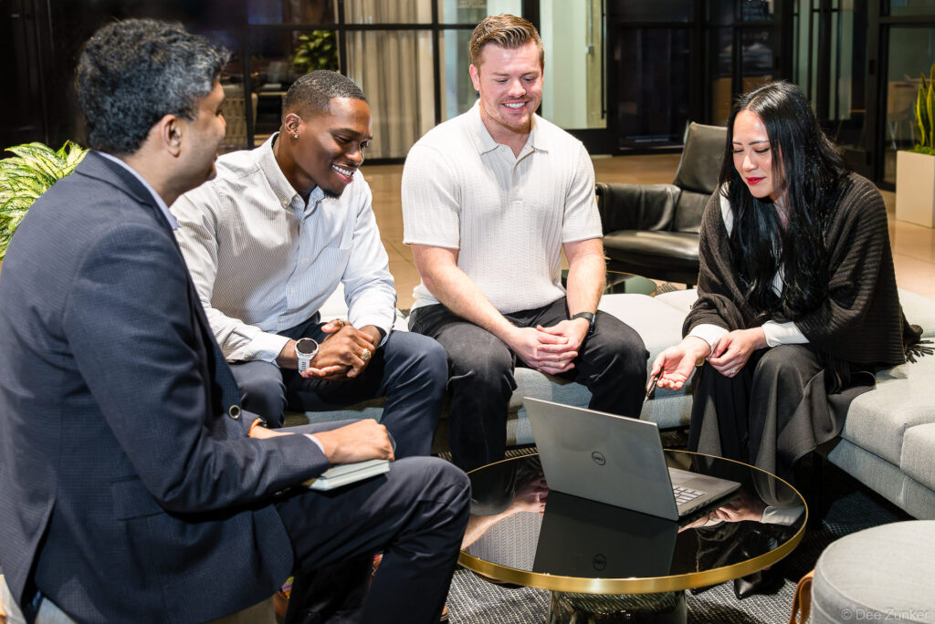 Four professionals in a casual Houston office lounge collaborate around a Dell laptop during a corporate branding photography session.