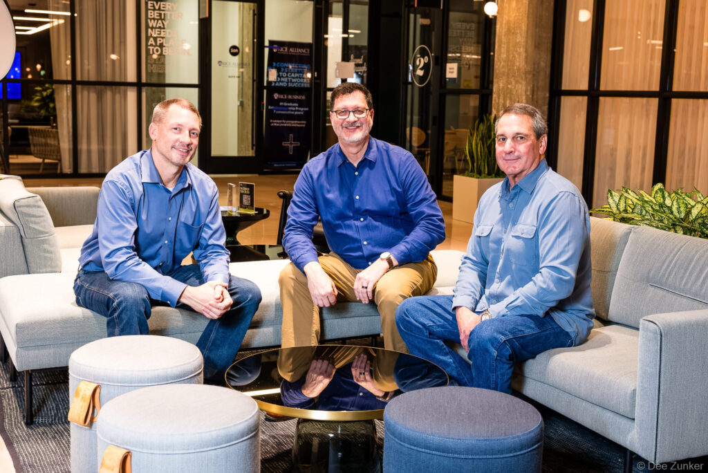 Three male business professionals in blue shirts seated in a modern Houston office lounge during a corporate team meeting, photographed by Dee Zunker Photography.