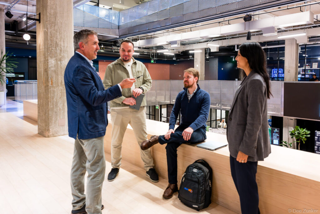 Four professionals in casual business attire collaborating in a modern open-plan Houston corporate office during a standing team meeting.