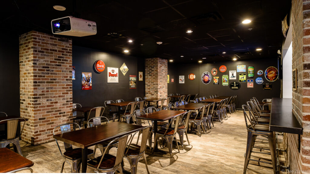 Industrial-style craft beer bar interior in Houston with brick columns, metal chairs, and vintage beer brand signs on dark walls
