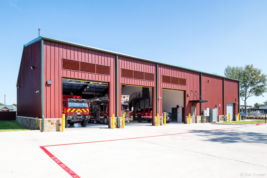 Exterior view of a red metal fire station with open bay doors revealing fire trucks inside, Crosby Texas