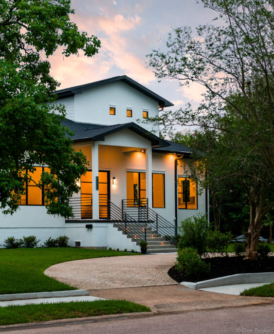 Custom luxury home exterior at twilight, Bellaire Texas, featuring modern farmhouse architecture with warm interior lighting and landscaped entry